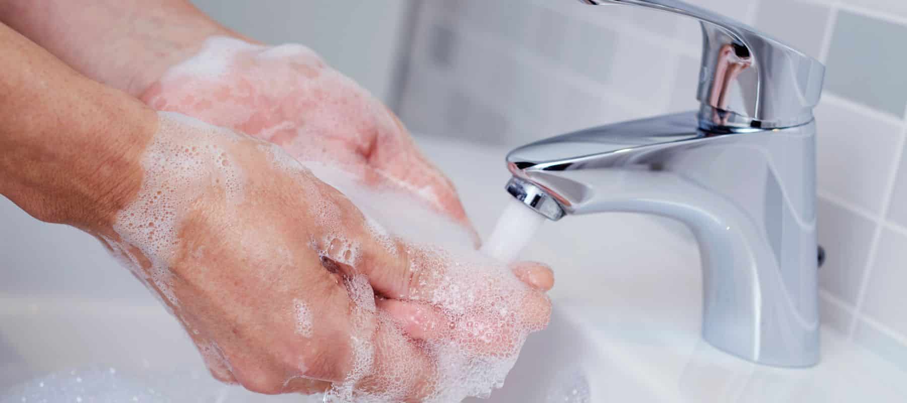 soapy hands washing under a stream of water frmo a bathroom faucet