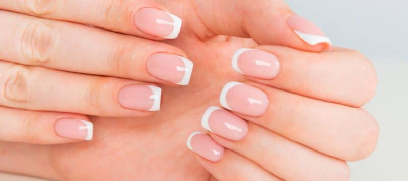 Close-up of hands with a French manicure, showcasing well-manicured nails with a light pink base and white tips.