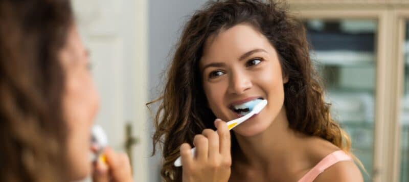 closeup of woman looking at herself in the mirror smiling while she brushes her teeth