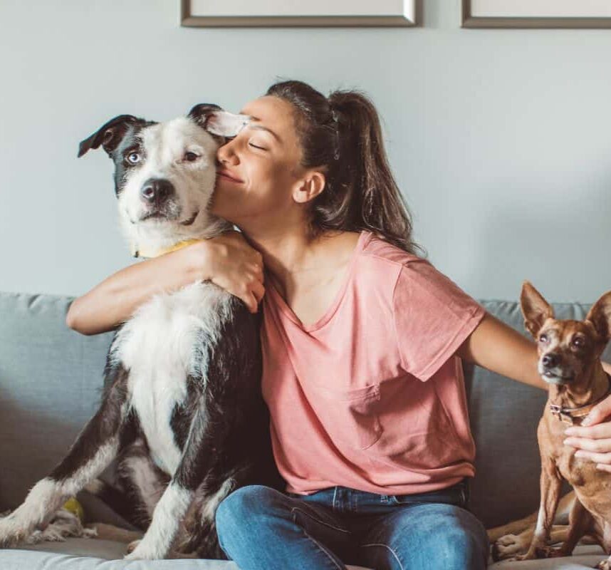 young woman sitting on a couch with her pets giving them kisses and pets